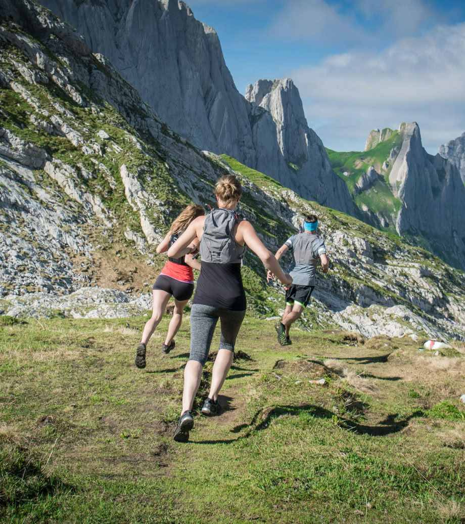 Trois personnes courant sur un sentier de montagne avec des falaises en arrière-plan.